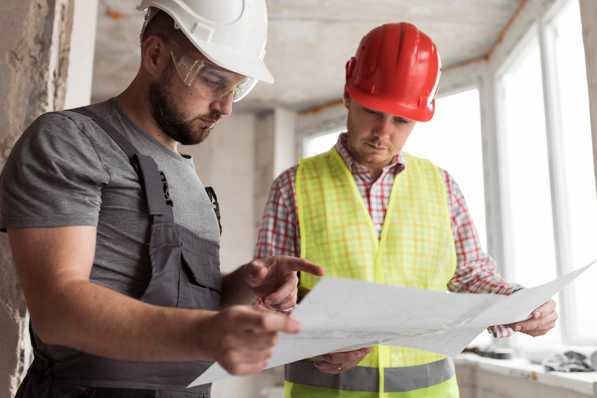 Twee bouwvakkers bespreken een bouwtekening op de werkplaats